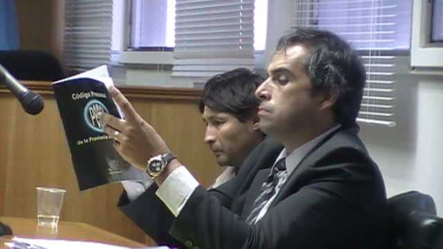 El defensor lee el código, a su lado Horacio Blanco escucha